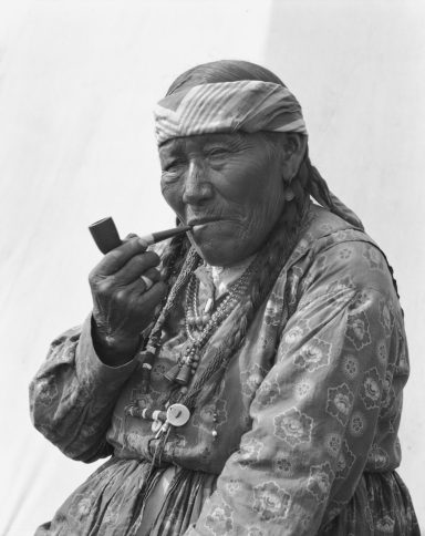 Elderly person with a pipe, wearing traditional clothing and accessories.