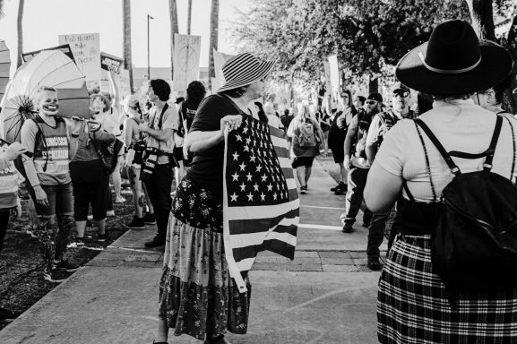 A crowd gathers at a rally, with one person holding an American flag.