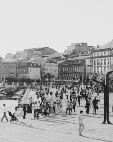 Busy urban plaza with people walking and buildings in the background, in black and white.